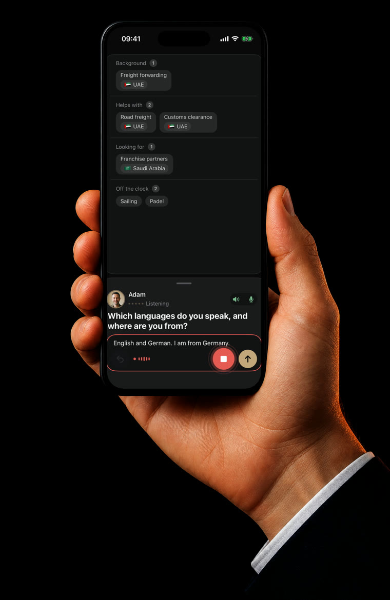 An iPhone in a hand, showing a talk with Adam, the profile assistant, while he fills in a profile.